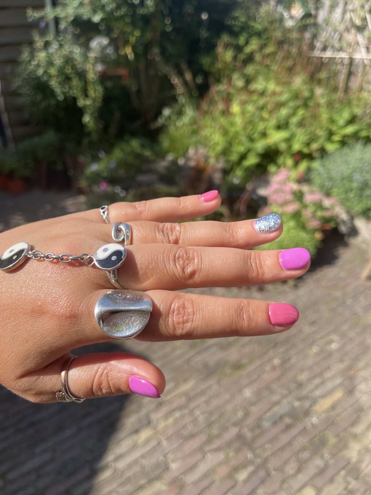 Hand met roze gelakte nagels, één zilveren glitternagel en zilveren ringen